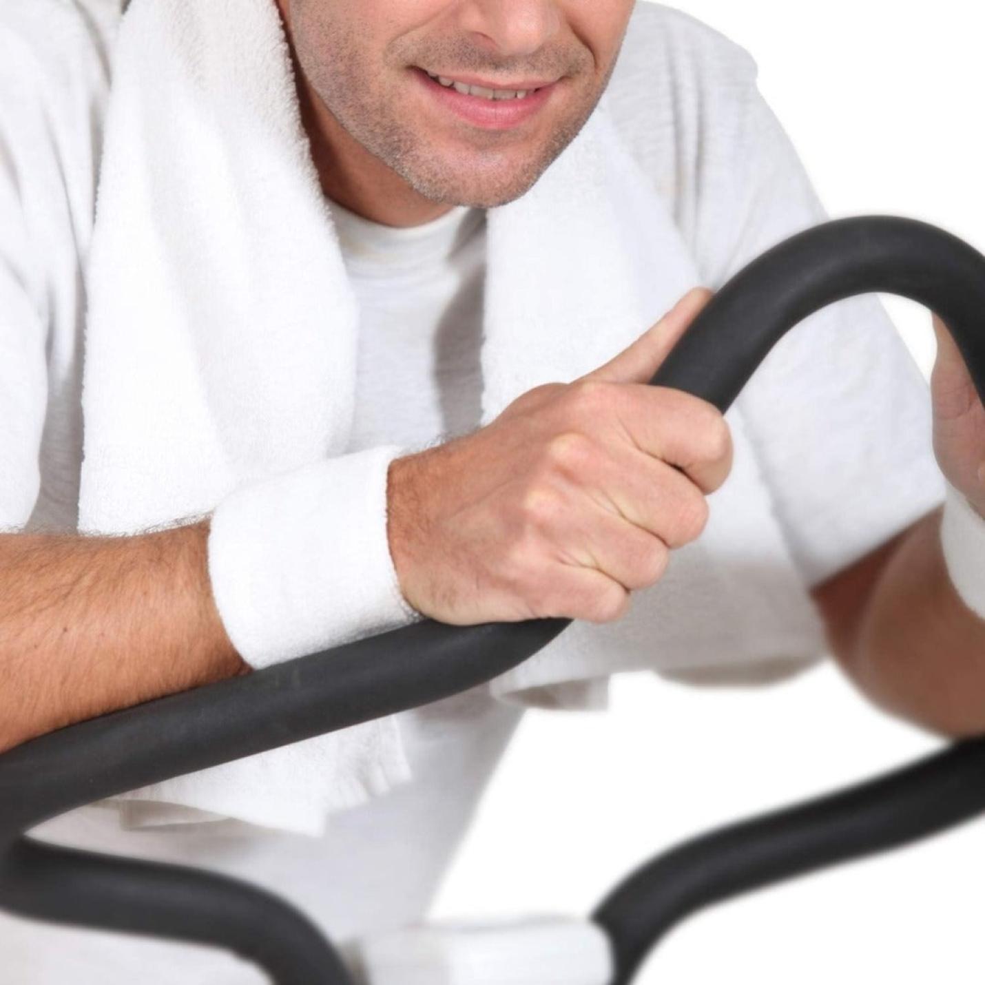 Man met een Zweetbandjes set voor basketbal, voetbal en atletiek om zijn nek aan het trainen op een hometrainer.