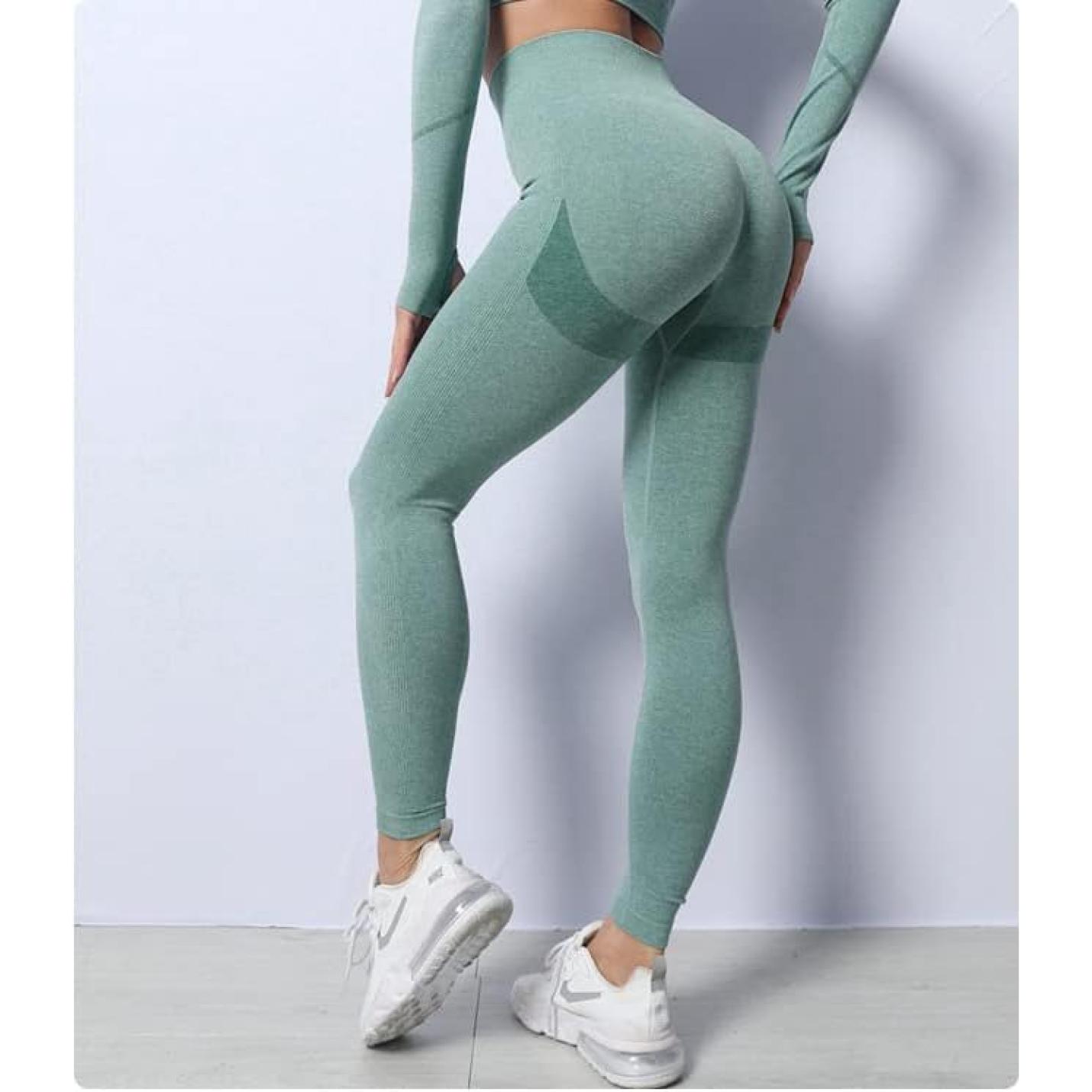 Vrouw in groene sportkleding, waaronder Zie er geweldig uit en voel je geweldig in deze 3-delige yoga workoutset, en witte sneakers poserend tegen een grijze achtergrond, waarbij de nadruk ligt op haar fitnesskleding.