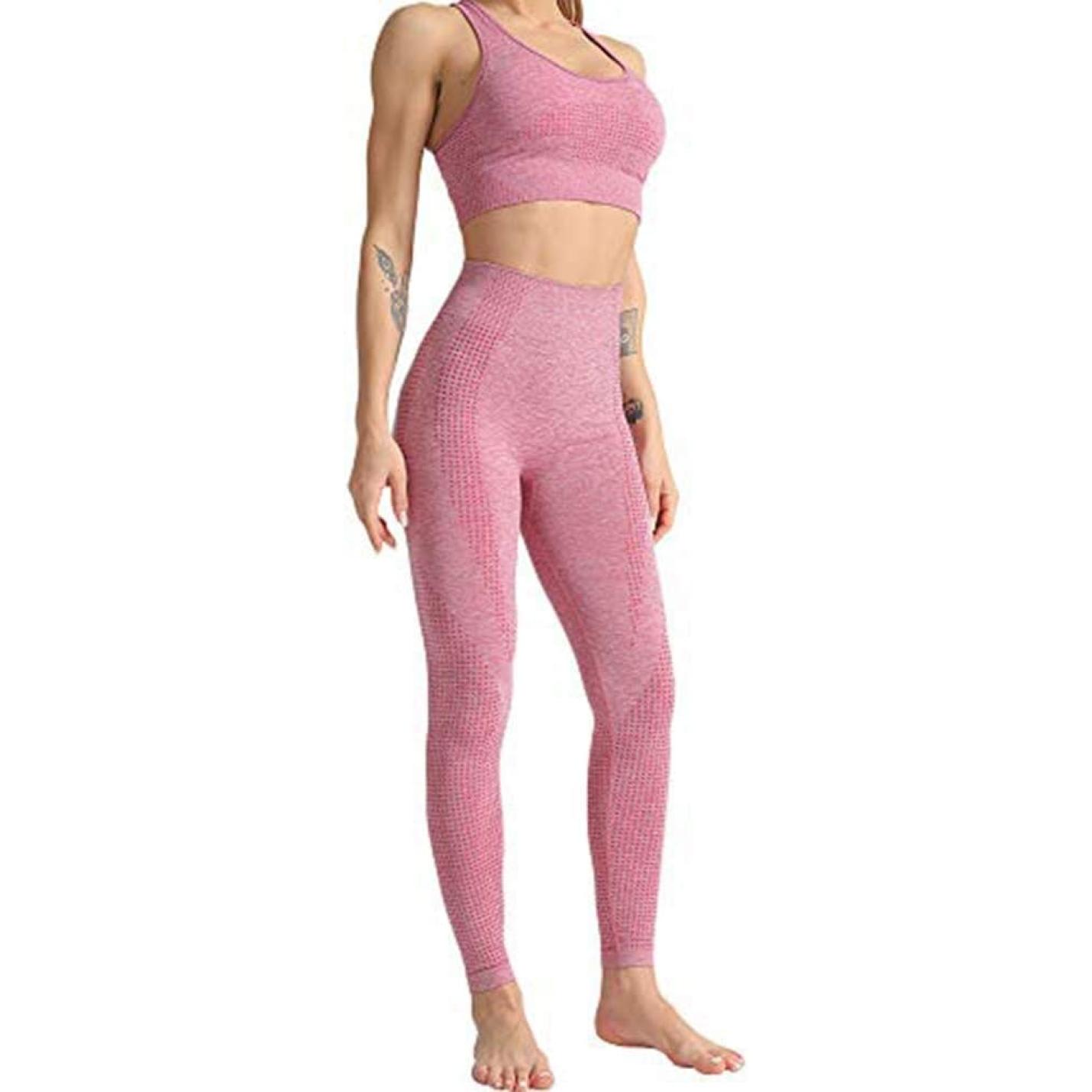 Een vrouw in roze sportkleding, waaronder een crop-top en naadloze legging met hoge taille, staat met haar handen op haar heupen, tegen een neutrale achtergrond.