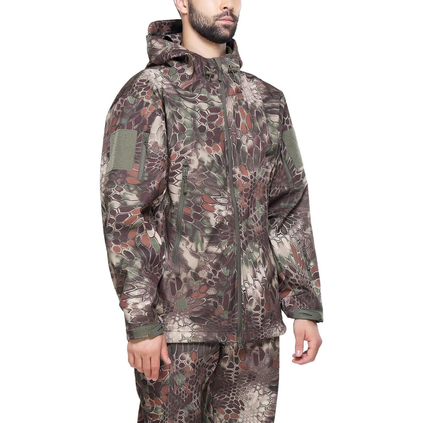 Een man, gekleed in een Camouflage tactische heren softshell jas met meerdere zakken en capuchon, staande tegen een effen achtergrond.