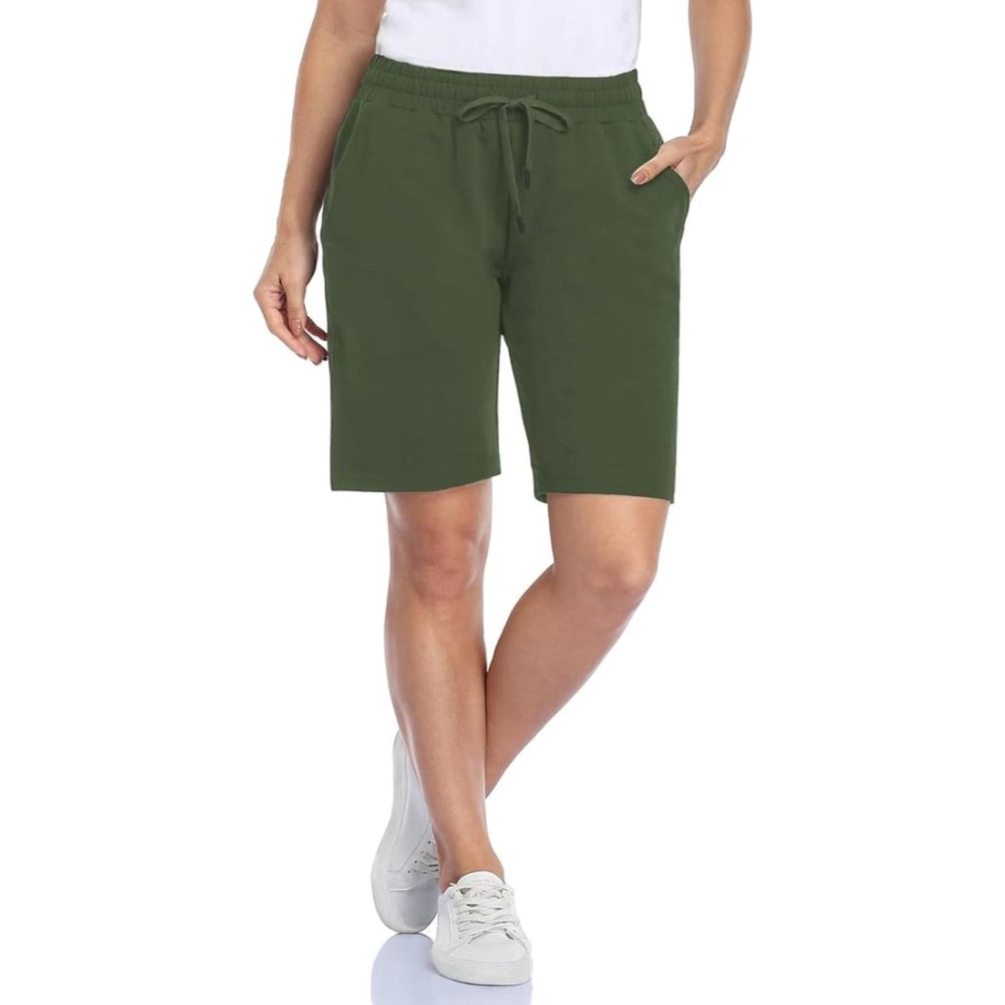 Staande vrouw in comfortabele olijfgroene Bermudashort voor dames en witte sneakers.