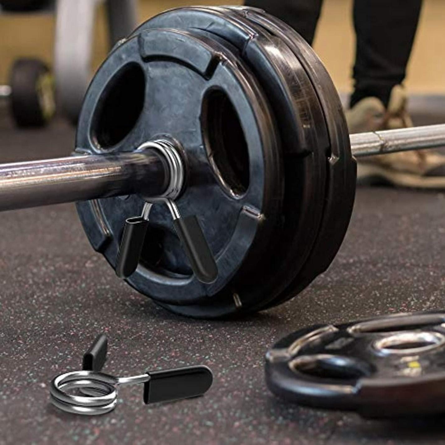 Barbell met grote halterschijven geladen, vastgezet met Halterklemmen voor dumbbells en halters, rustend op een gymvloer met meer gewichten en apparatuur in de buurt.