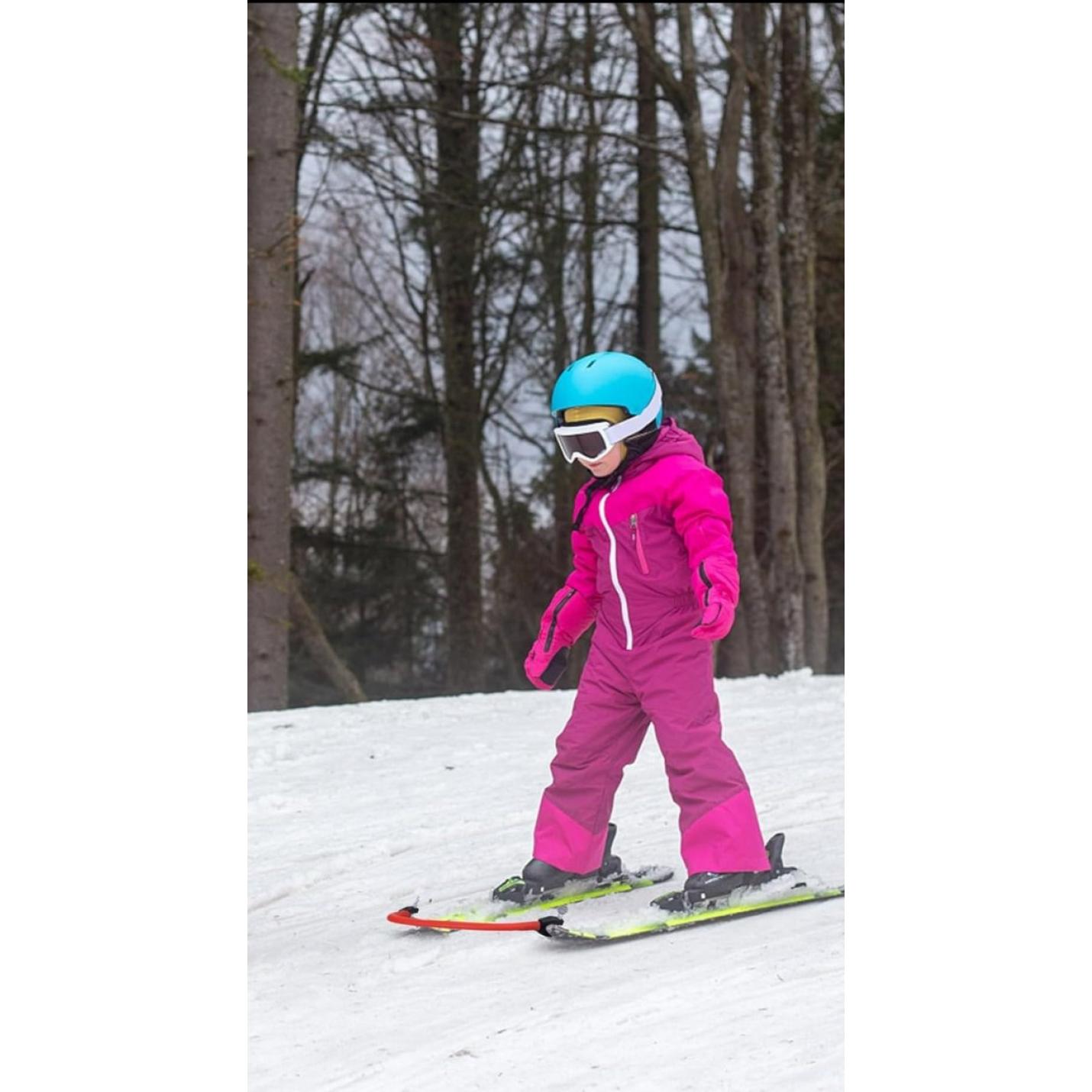 Een persoon in een roze skipak en blauwhelm die aan het skiën is op een besneeuwde heuvel met bomen op de achtergrond, en laat zien hoe Leer je kinderen skiën effectief met deze skitipconnector werkt.