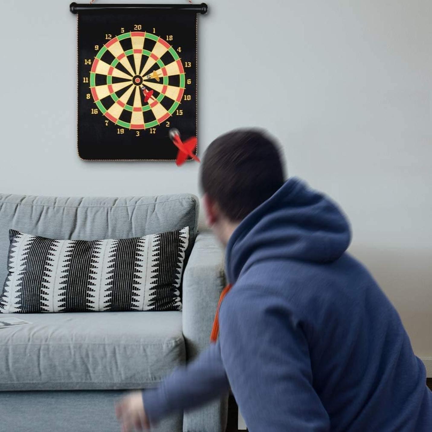 Man die binnenshuis dart speelt met een Dubbelzijdig magnetisch dartbord aan de muur.