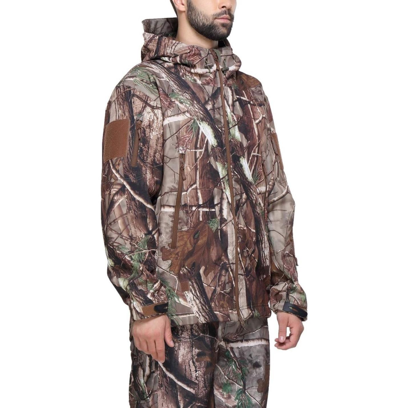 Man met een Camouflage tactische heren softshell jas met capuchon, voorzien van een bosmotief en een bruine patch op de mouw. Deze heren softshell jas is bovendien ademend en waterdicht.