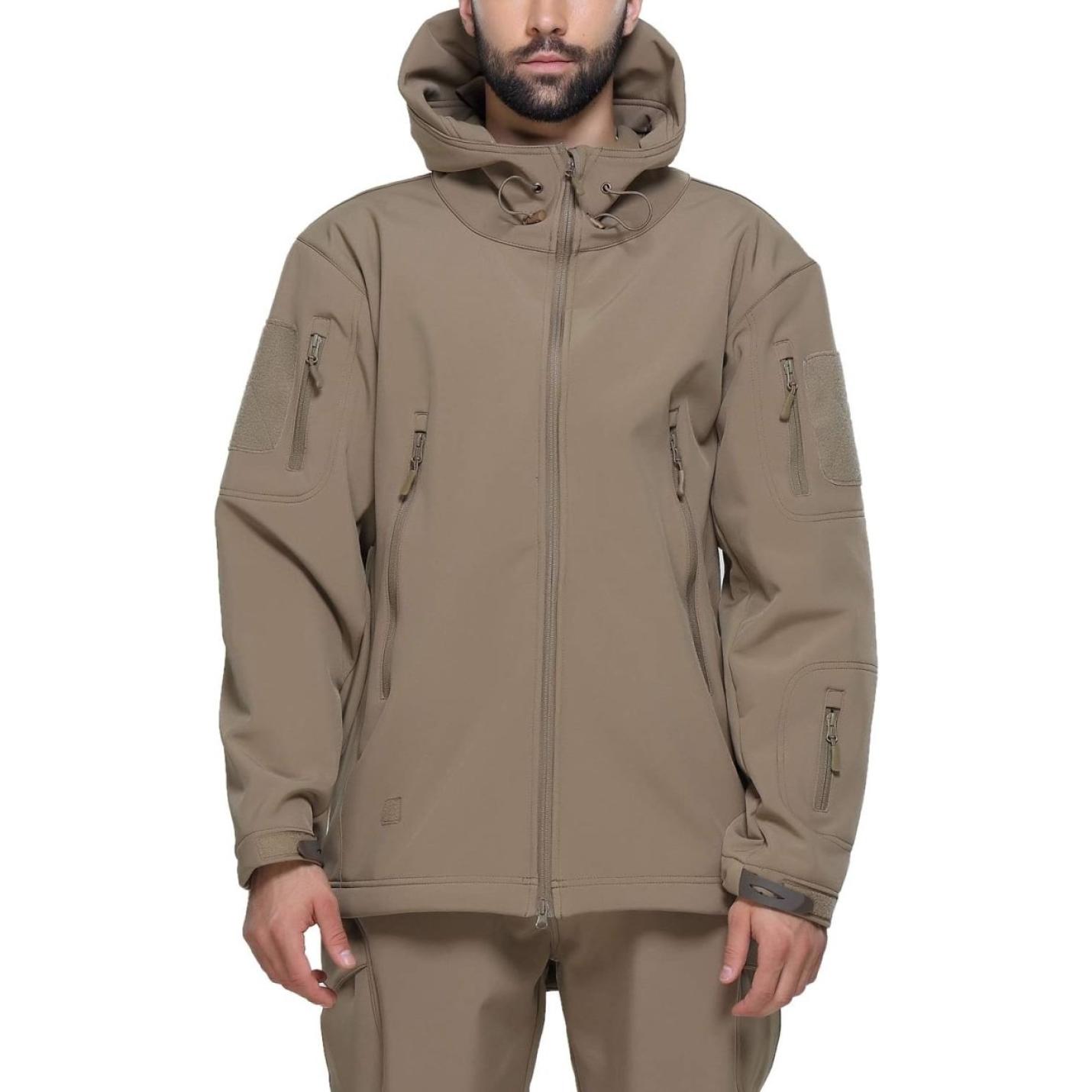 Een man draagt een camouflage tactische heren softshell jas met meerdere zakken met ritssluiting, een capuchon en staat met zijn handen iets open.