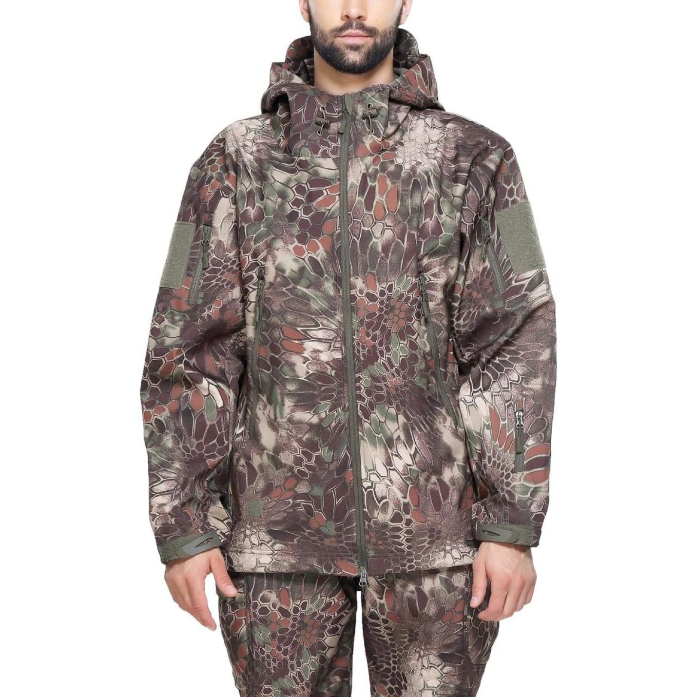 Man met een camouflage tactische heren softshell jas met capuchon, staande met de handen iets uitgestrekt, tegen een effen achtergrond.