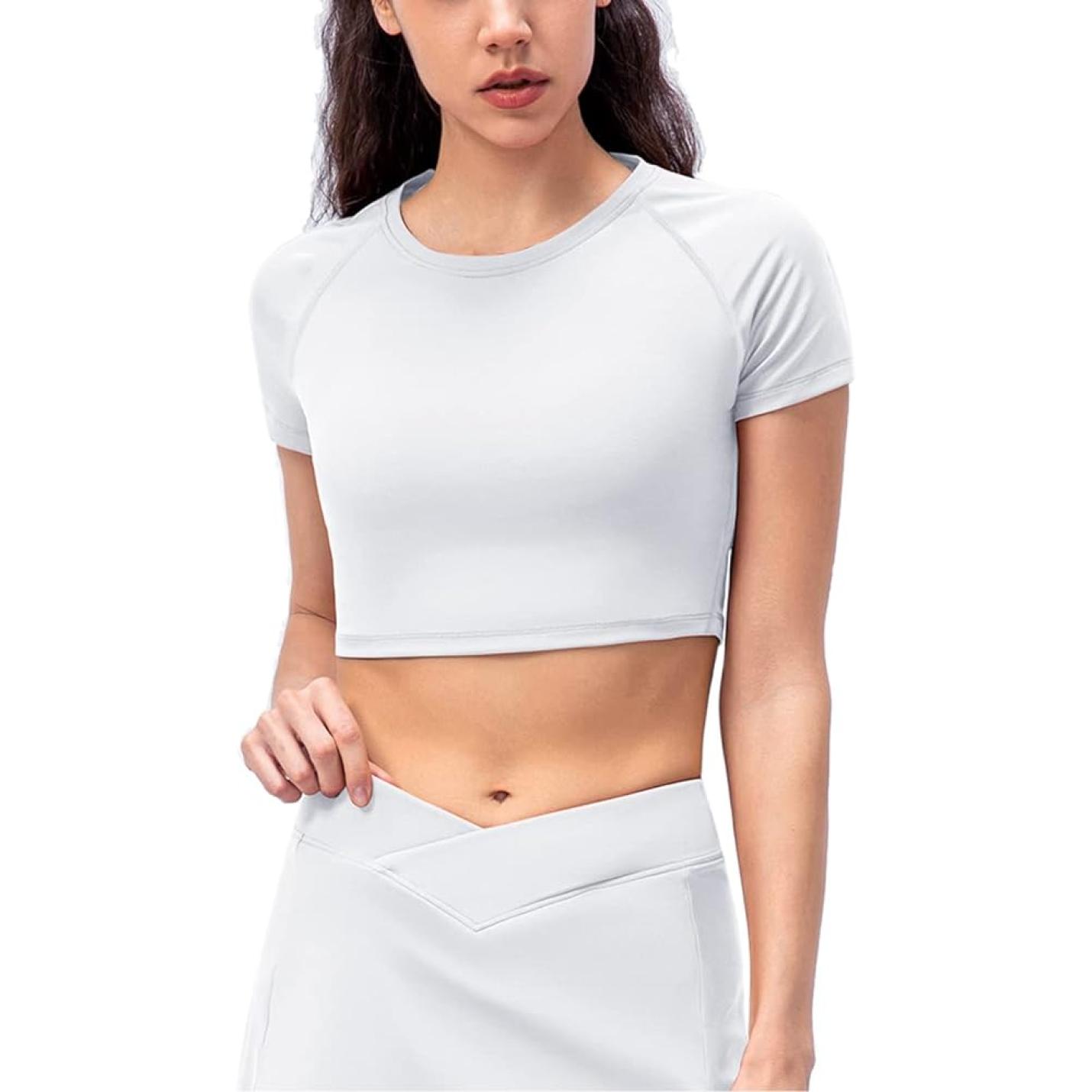 Een vrouw in een witte Naadloze dames fitness crop top en bijpassende broek met hoge taille, poserend met één hand op haar heup.