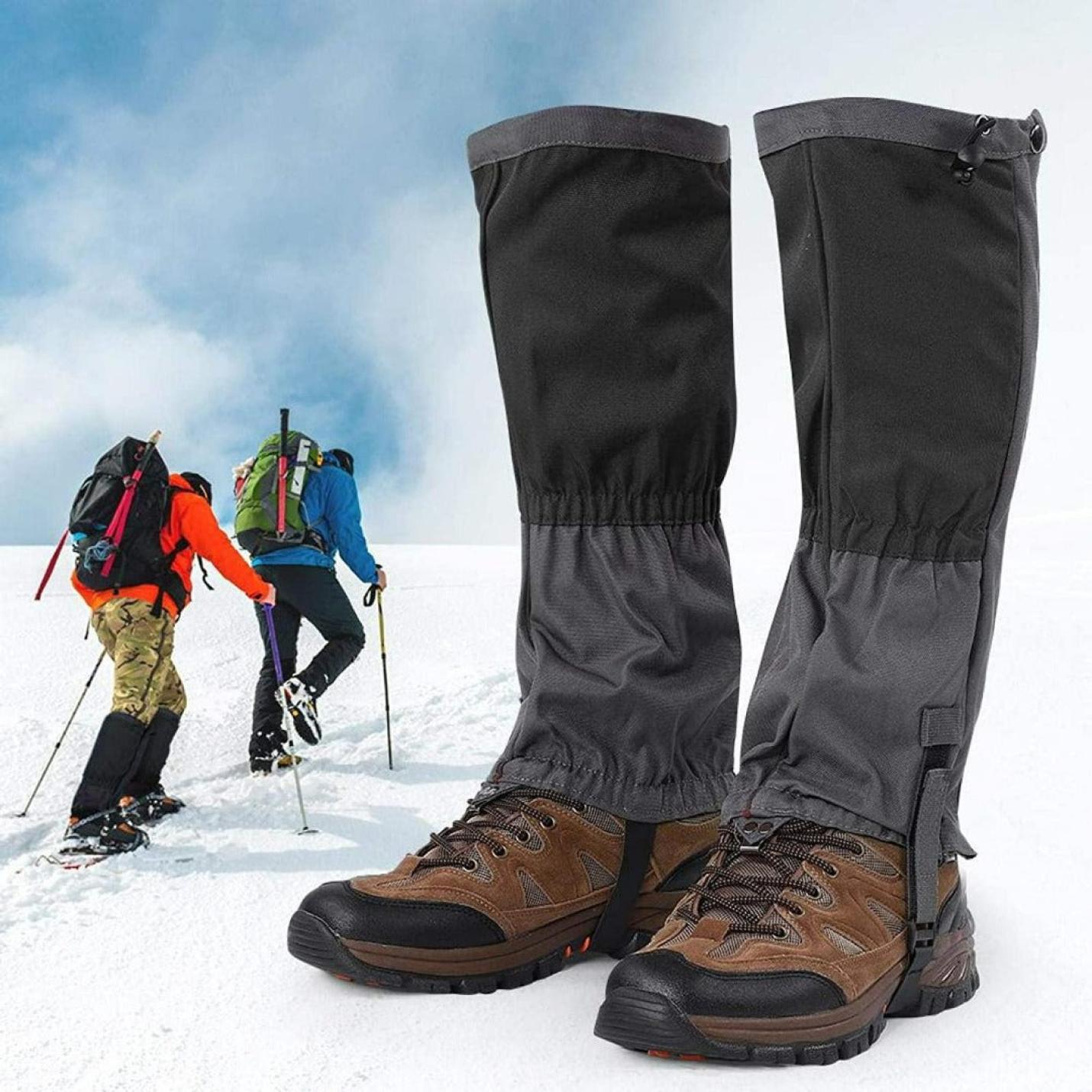 Op de voorgrond beenkappen vastgemaakt aan wandelschoenen, met op de achtergrond twee wandelaars die door besneeuwd terrein trekken, gekleed in Ontdek het ultieme comfort en bescherming met onze sneeuw gamaschen voor volwassenen.