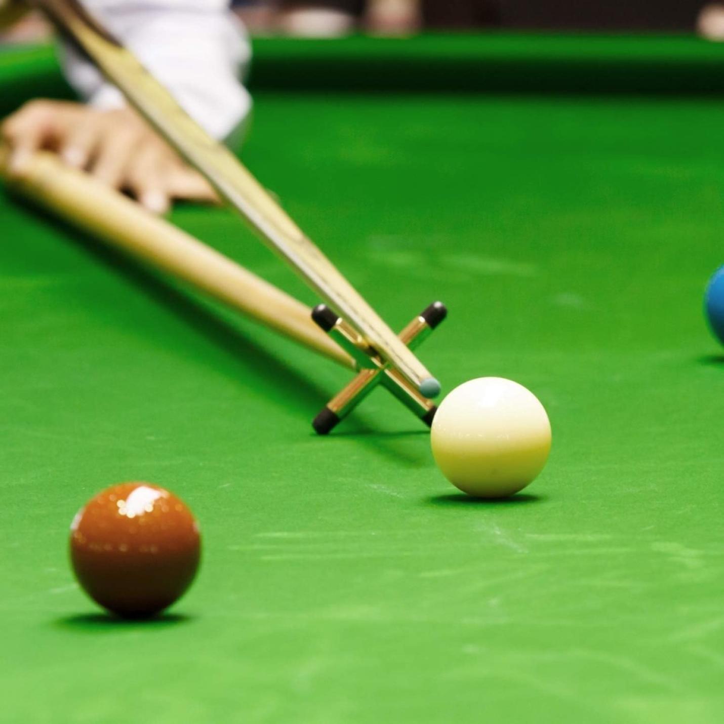 Een speler die een schot in snooker opstelt en een rust gebruikt om over de witte speelbal te overbruggen op een snookertafelsteunen: verbeter je spel met precisie en stabiliteit met deze keubruggen.