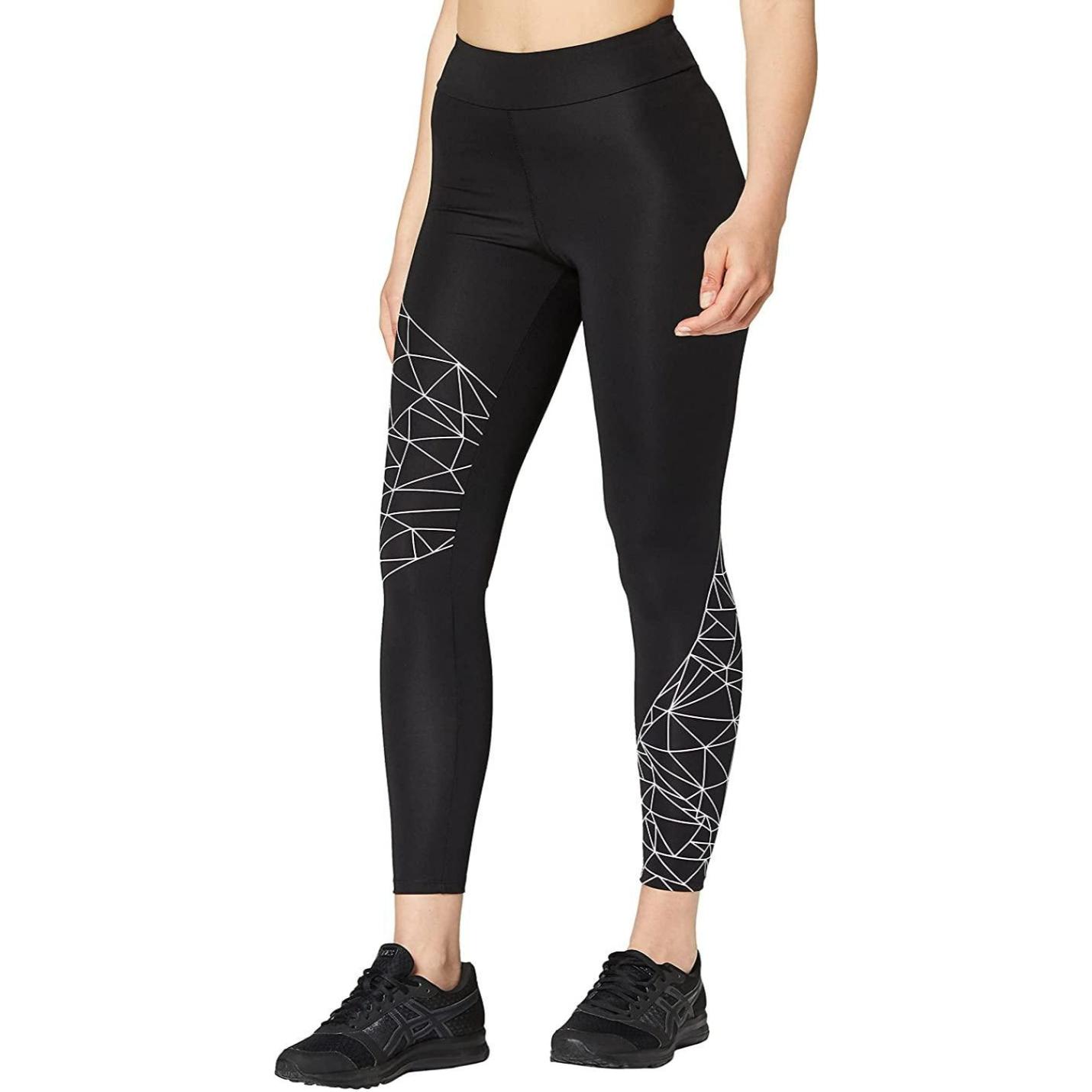 Een staande vrouw in zwarte ultra stretch Ervaar comfort en stijl met onze sportlegging voor dames met een wit geometrisch patroon, gecombineerd met zwarte sneakers.