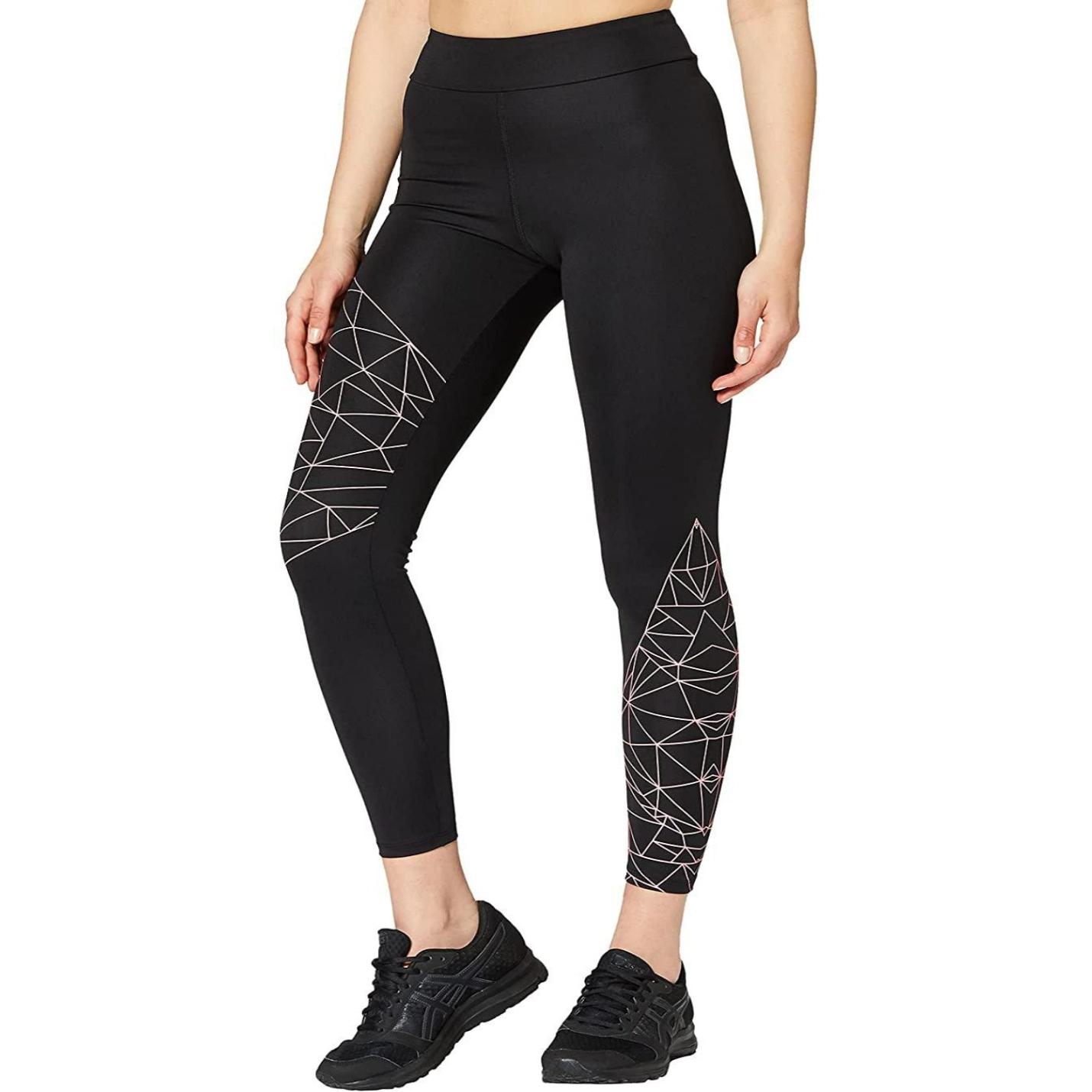 Vrouw draagt Comfort + Stijl sportlegging voor dames met zwarte kleur, versierd met witte geometrische patronen aan de gedekt, gecombineerd met zwarte sneakers, staande tegen een witte achtergrond.