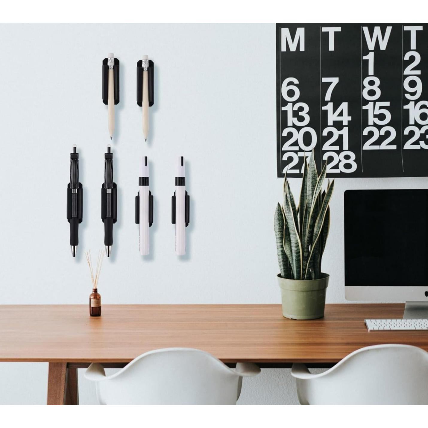 Een minimalistische werkplek met een iMac, een kalender aan de muur, Verleidelijke siliconen penhouders op het bureau, een potplant en twee stoelen.