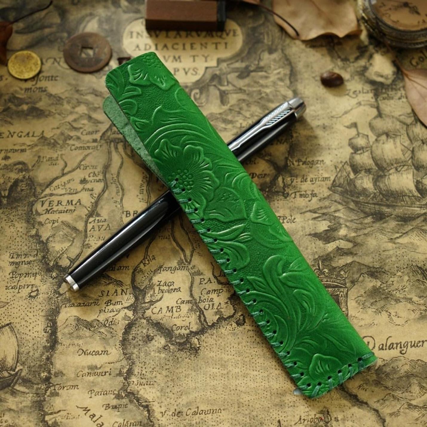 Een universele pasvorm groene leren etui met bloemenpatroon in reliëf, rustend op een vintage kaart. Vintage lederen pennenhouder: de perfecte manier om uw pennen te beschermen en te stylen